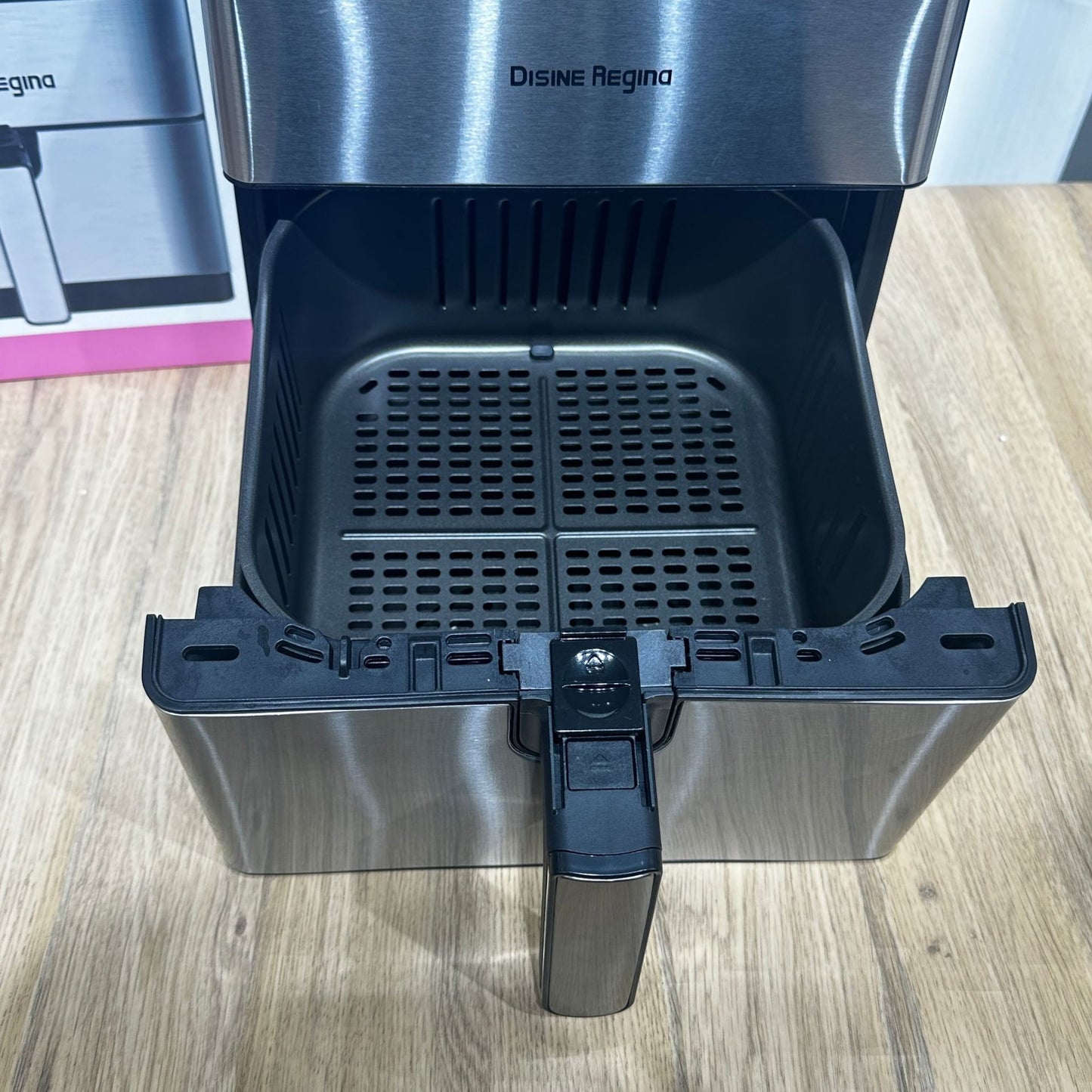 Stainless steel appliance with open compartment on a wooden surface, brand 'Disine Regina' visible.