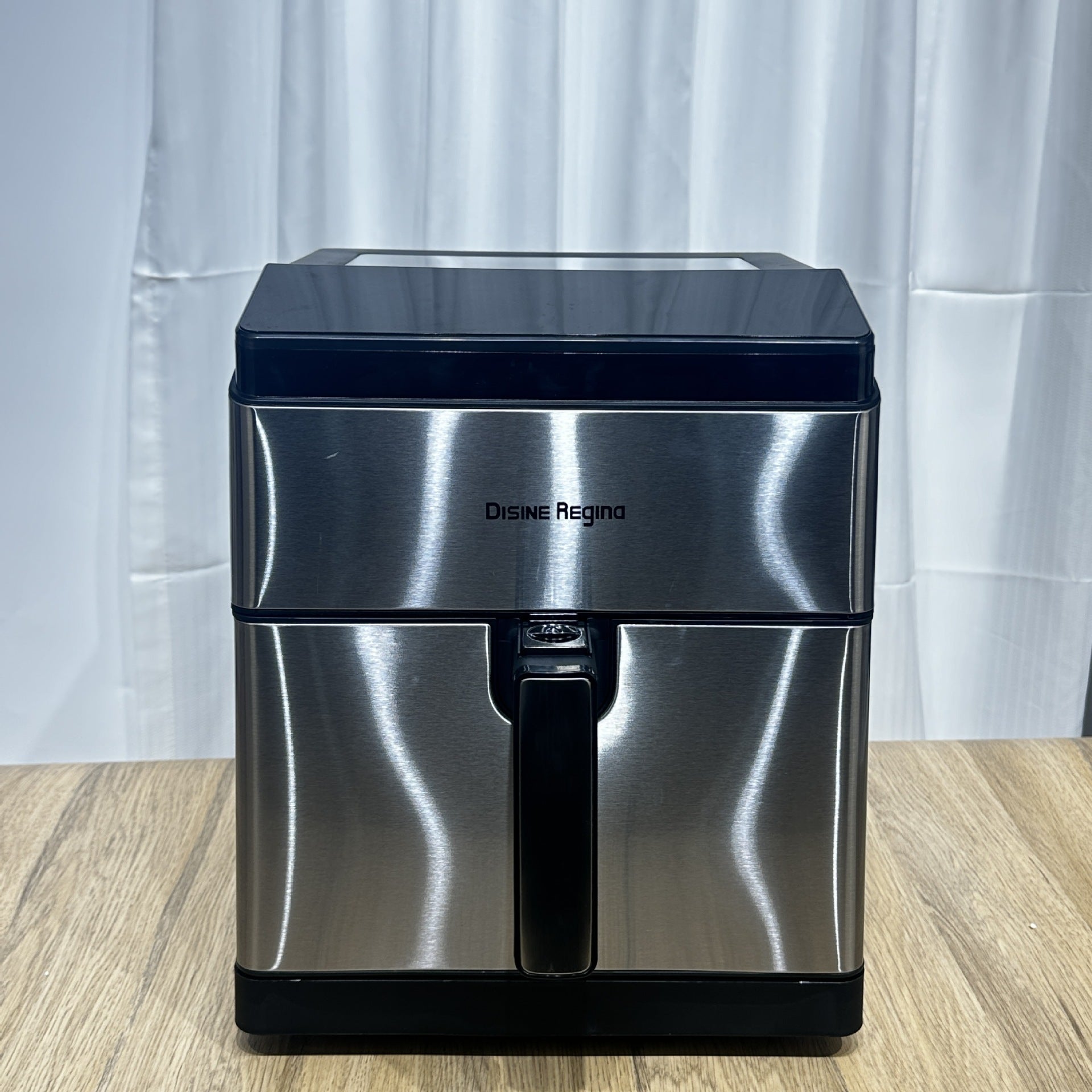 Stainless steel air fryer with black accents on a wooden surface and white curtain background