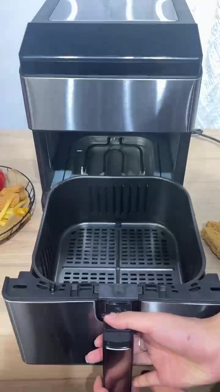 Black air fryer with a person holding it open on a wooden surface.