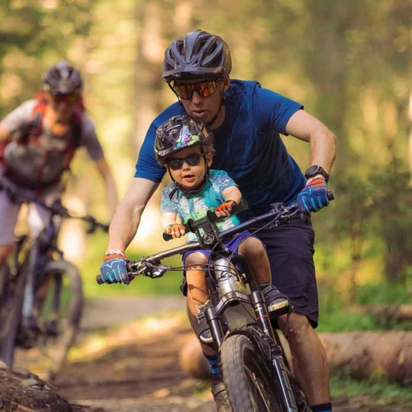 Man and child riding bicycles on a trail with another cyclist in the background.